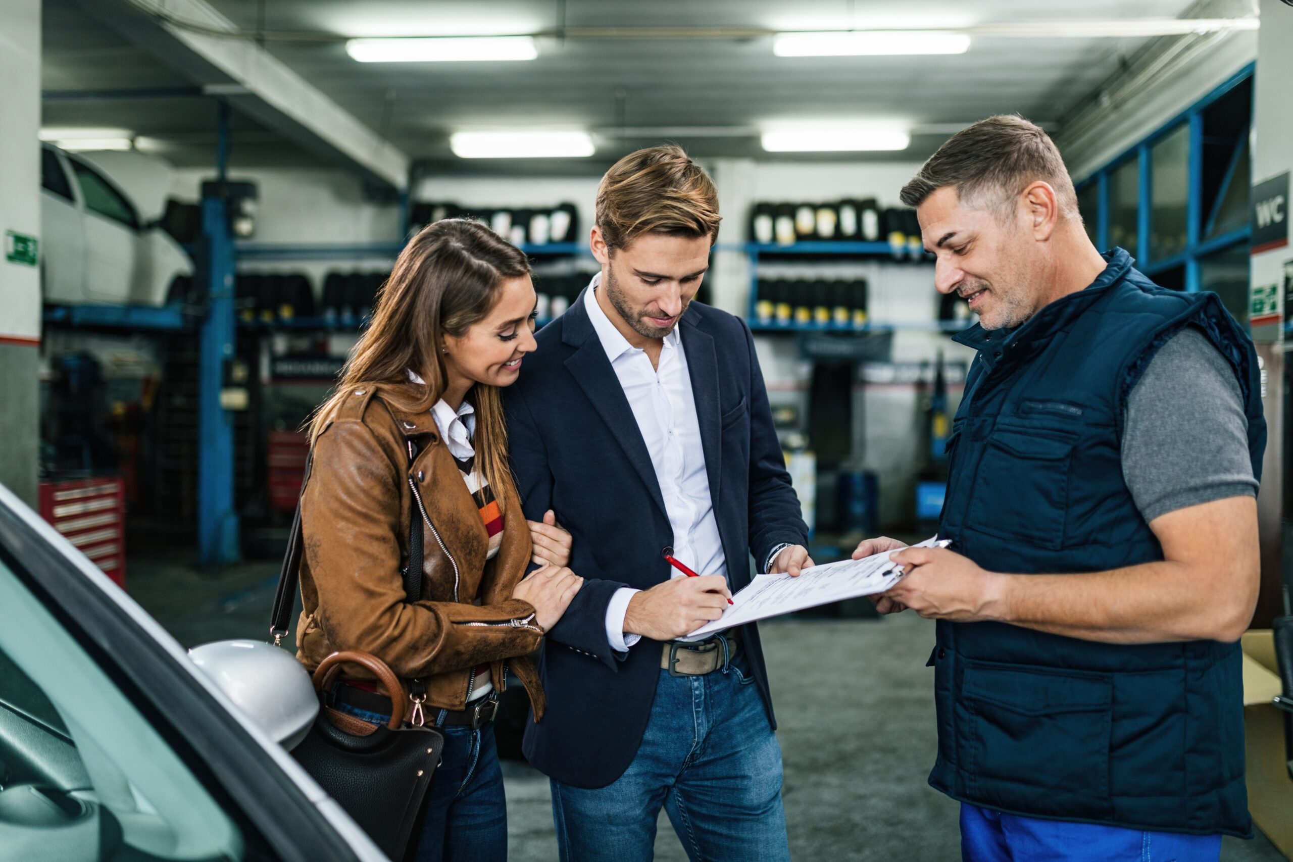 young-happy-couple-signing-documents-while-being-with-car-mechanic-repair-shop (1)